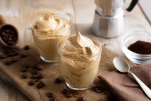 Crema al caffè spumosa fatta in casa in un bicchiere trasparente, guarnita con granella di caffè, su superficie di marmo chiaro