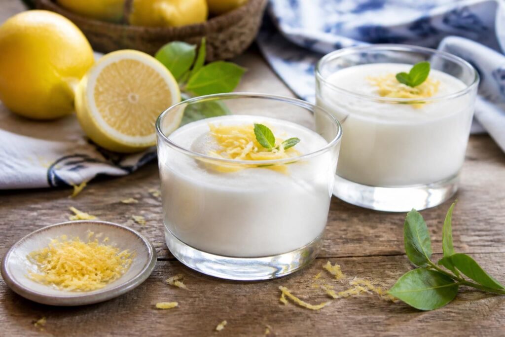 Gelo di limone siciliano senza uova servito in coppette di vetro, decorato con scorza di limone e pistacchio di Bronte tritato, su un tavolo di legno chiaro