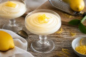Crema al limone con latte condensato senza cottura servita in coppette di vetro, con scorza di limone grattugiata e foglioline di menta fresca