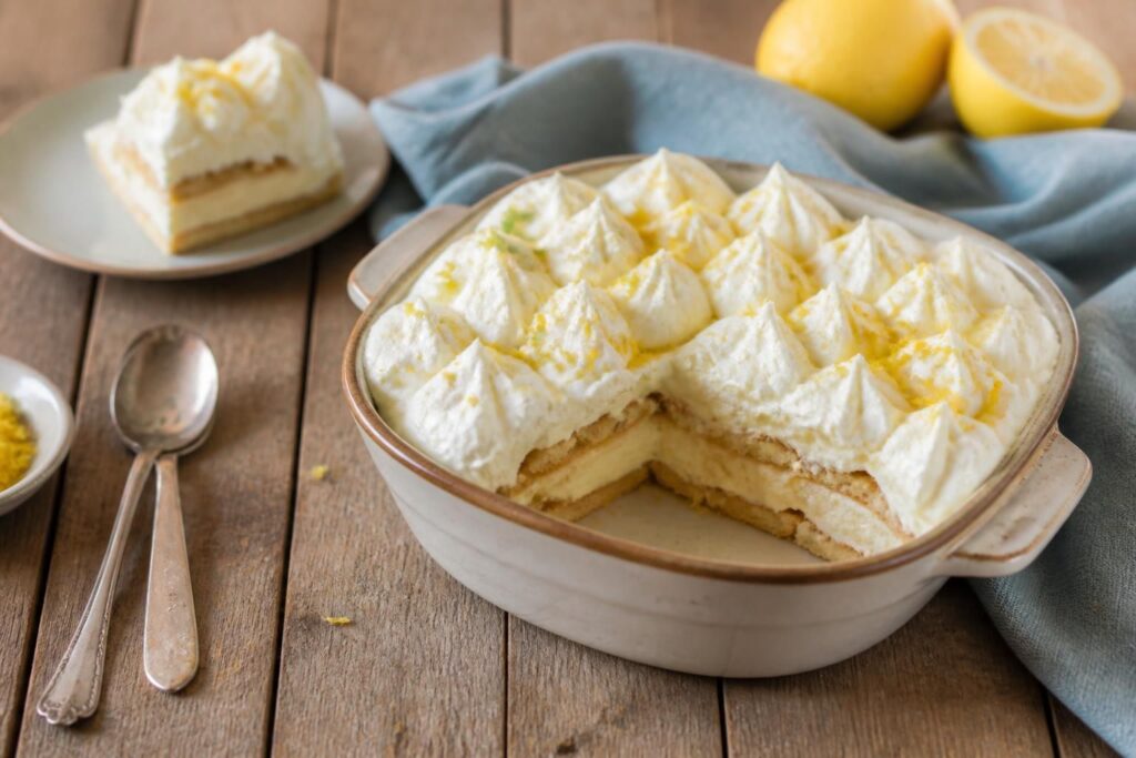 Tiramisù al limone senza uova con savoiardi, crema al mascarpone e scorza di limone bio, servito in coppette individuali su sfondo estivo chiaro
